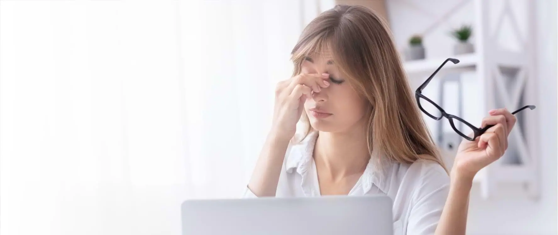 Frau hält eine schwarze Brille in der Hand und arbeitet konzentriert am Laptop